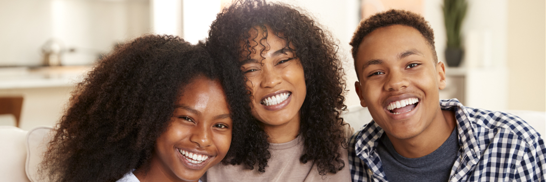 Mother and two teenage children smiling together at home, showing healthy white teeth