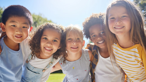 Five diverse smiling children hugging outdoors on a sunny day in Fort Collins