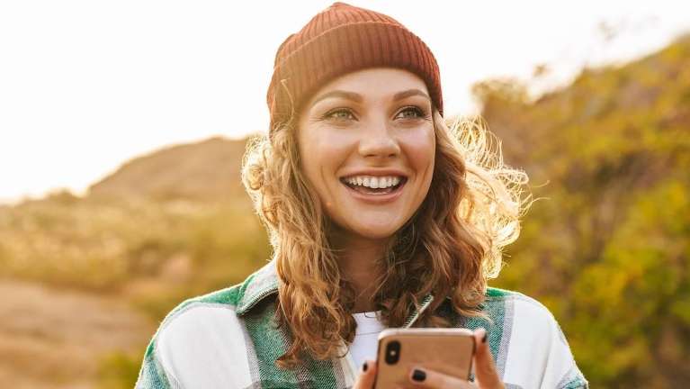 Woman with beanie smiling outside holding her phone, fort collins co