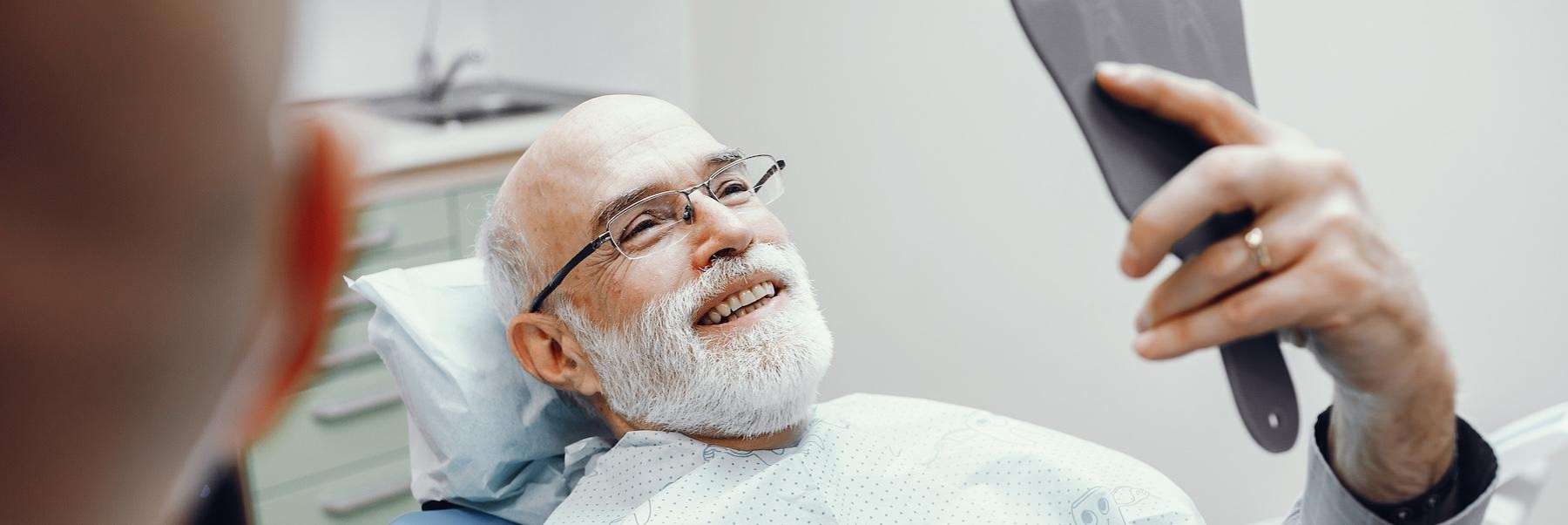 Older man smiling in dental chair looking at dental implant, fort collins co 